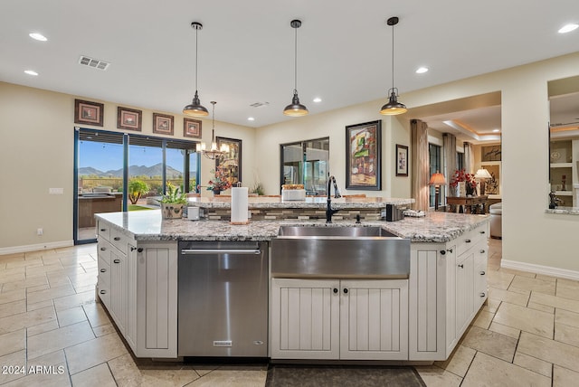 kitchen featuring white cabinets, hanging light fixtures, light stone counters, a kitchen island with sink, and sink