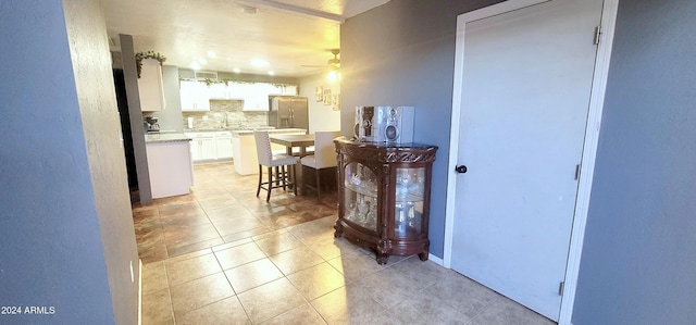 kitchen with stainless steel fridge, backsplash, ceiling fan, white cabinets, and a breakfast bar area