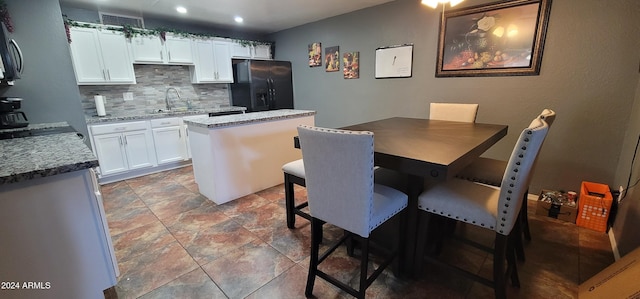 kitchen featuring light stone countertops, a kitchen island, black fridge, backsplash, and white cabinets