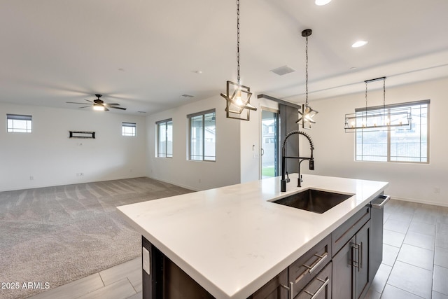 kitchen featuring decorative light fixtures, a center island with sink, light countertops, and a sink