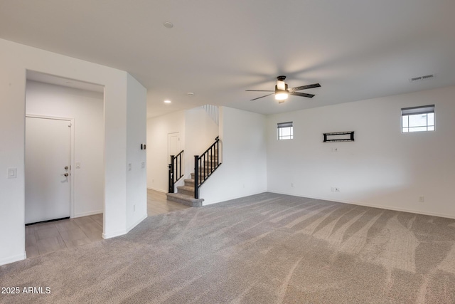 interior space featuring visible vents, light colored carpet, stairs, and a ceiling fan