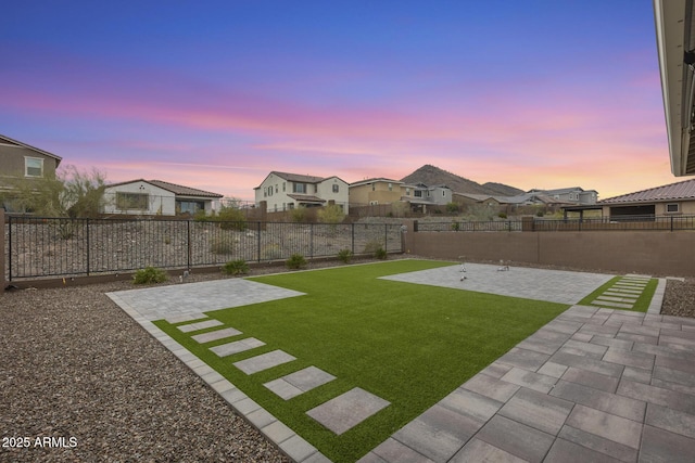 yard at dusk with a patio area, a residential view, and a fenced backyard