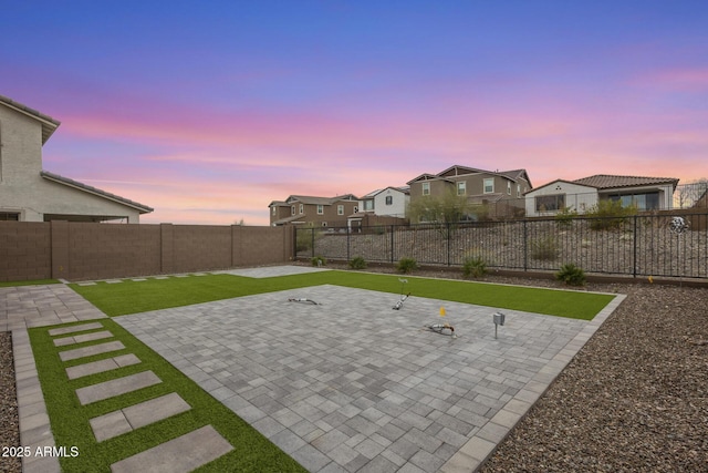 patio terrace at dusk featuring a fenced backyard, a residential view, and a lawn