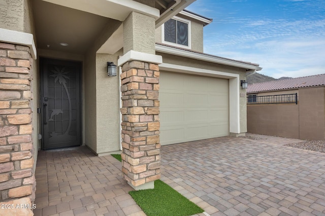 entrance to property with a garage, fence, stone siding, and stucco siding