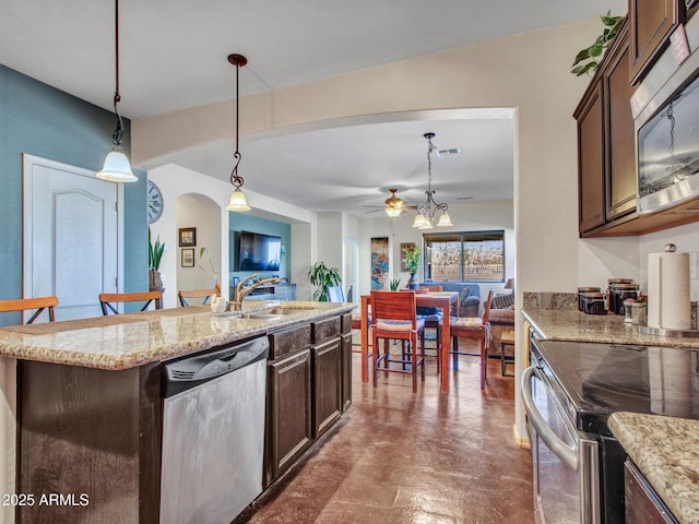 kitchen with arched walkways, appliances with stainless steel finishes, a sink, and dark brown cabinetry