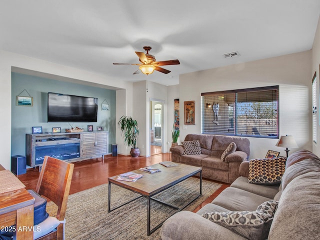 living room with a ceiling fan, visible vents, a fireplace, and wood finished floors