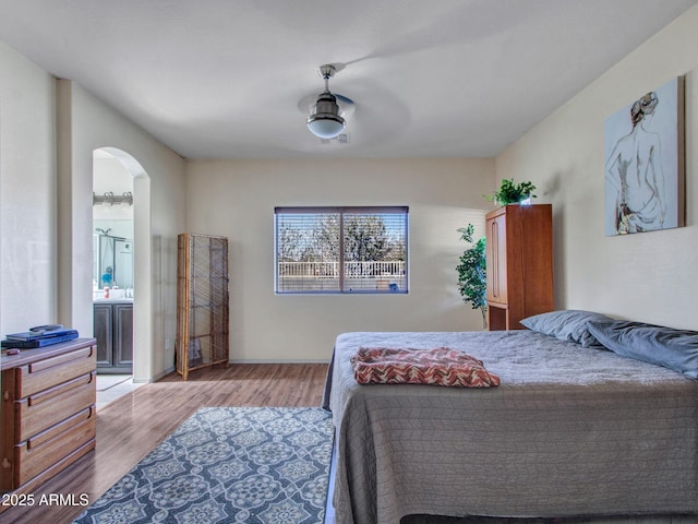 bedroom with arched walkways, light wood finished floors, visible vents, a ceiling fan, and ensuite bath