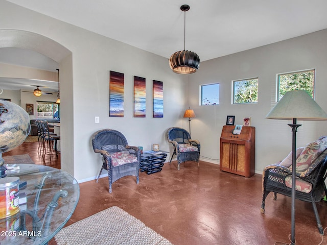 living area with arched walkways, a ceiling fan, and baseboards