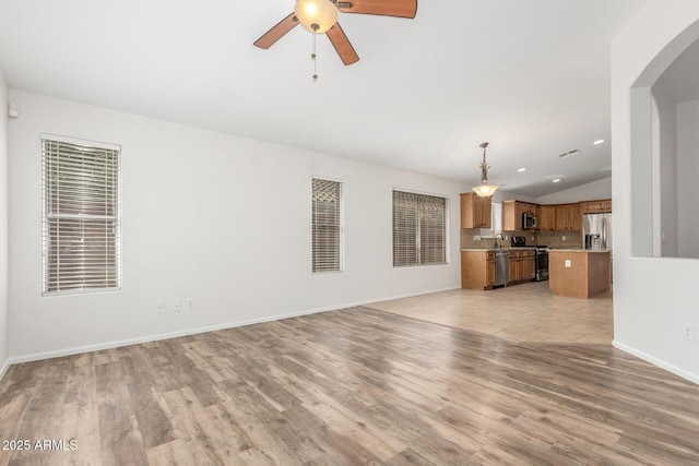 unfurnished living room with lofted ceiling, a ceiling fan, arched walkways, baseboards, and light wood-style flooring