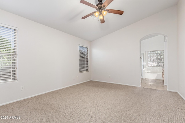spare room featuring light carpet, vaulted ceiling, baseboards, and arched walkways