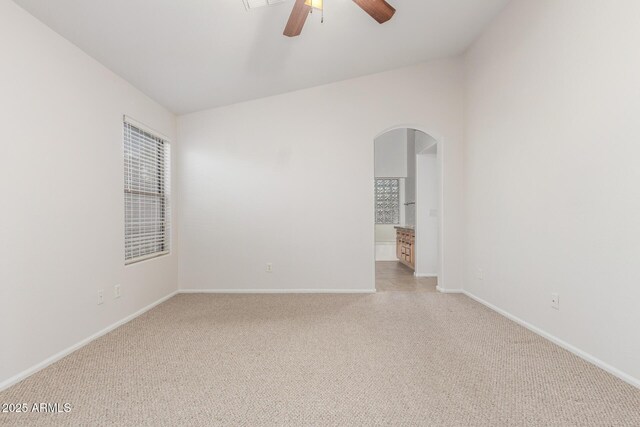 unfurnished room with baseboards, arched walkways, a ceiling fan, and light carpet