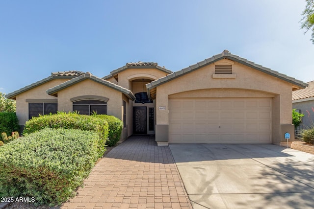 mediterranean / spanish house with stucco siding, a tile roof, an attached garage, and concrete driveway