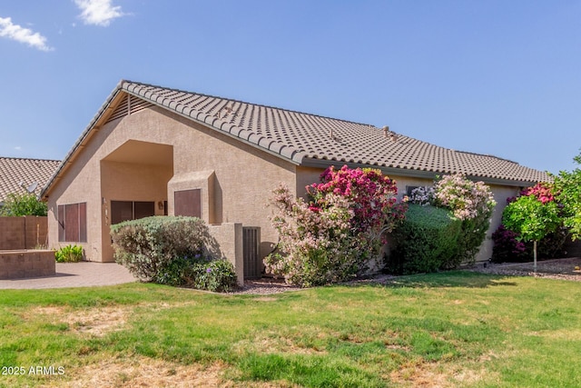 view of home's exterior with a yard, a tile roof, stucco siding, and fence