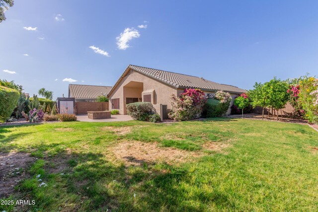 back of property featuring a tile roof, fence, a yard, a patio, and stucco siding