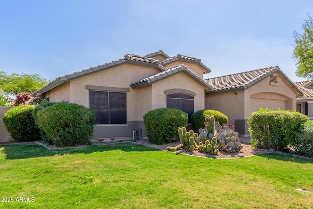 mediterranean / spanish house featuring stucco siding, an attached garage, a tile roof, and a front lawn