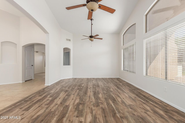 unfurnished living room with arched walkways, a ceiling fan, and high vaulted ceiling