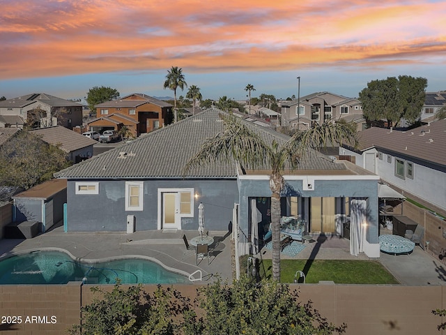 back house at dusk featuring a patio area and a fenced in pool