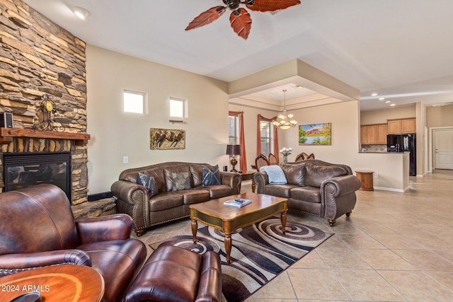 living room with light tile patterned floors, a stone fireplace, and ceiling fan with notable chandelier