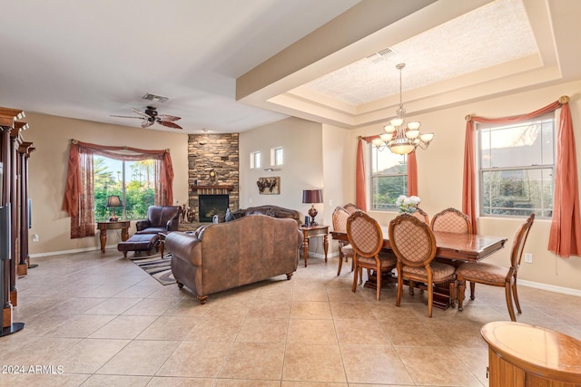 tiled dining space featuring a stone fireplace, ceiling fan with notable chandelier, and a tray ceiling