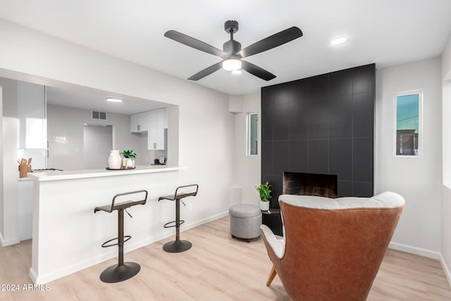 interior space featuring a fireplace, ceiling fan, light hardwood / wood-style floors, and white cabinets