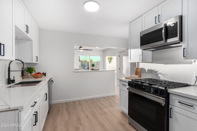 kitchen with stainless steel appliances, light hardwood / wood-style floors, sink, light stone counters, and white cabinets