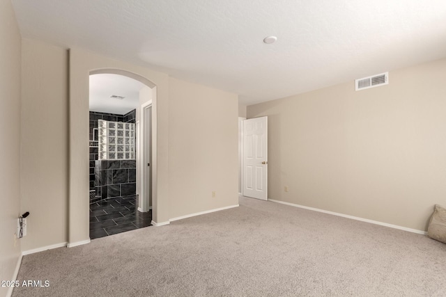 empty room featuring carpet flooring, arched walkways, and baseboards
