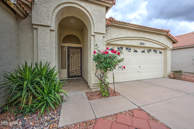 view of exterior entry featuring stucco siding, a garage, and concrete driveway