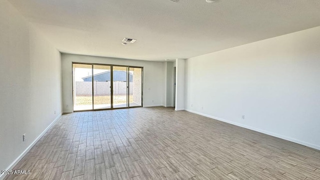 spare room with light wood-style flooring, a textured ceiling, visible vents, and baseboards