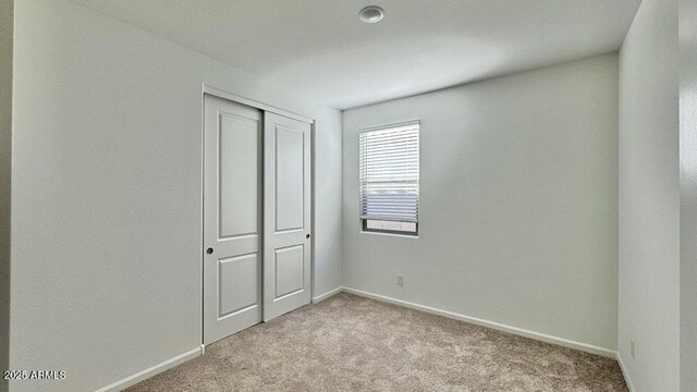 unfurnished bedroom with a closet, light colored carpet, and baseboards