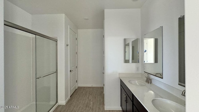 full bath with double vanity, a shower with door, a sink, and wood finished floors