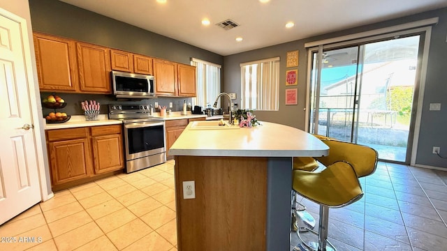 kitchen with appliances with stainless steel finishes, a kitchen island with sink, sink, and light tile patterned floors