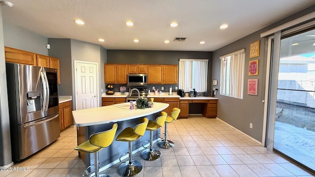 kitchen with stainless steel appliances, light tile patterned flooring, a breakfast bar area, and a center island with sink