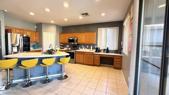 kitchen with light tile patterned floors, sink, appliances with stainless steel finishes, a kitchen breakfast bar, and an island with sink