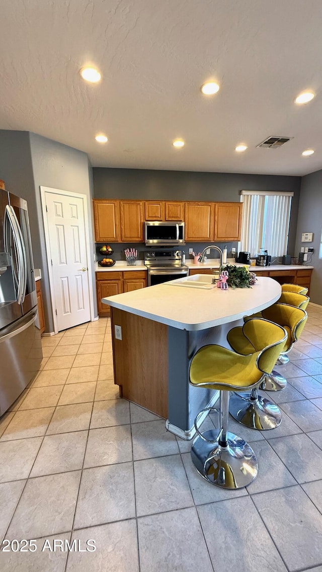 kitchen featuring light tile patterned flooring, a breakfast bar, sink, an island with sink, and stainless steel appliances