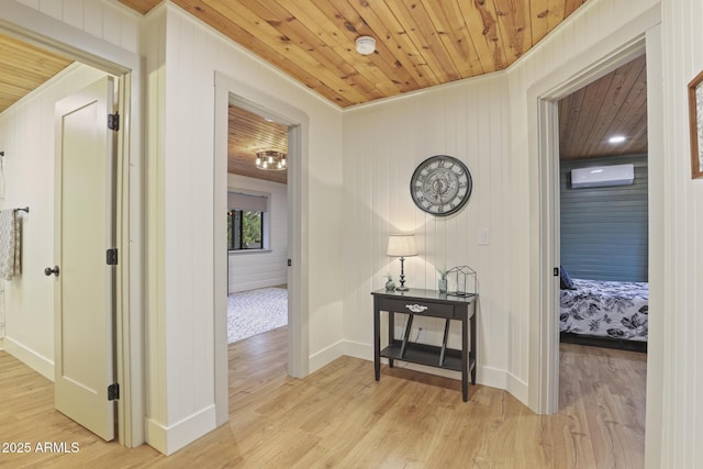 corridor with wooden ceiling, light wood-type flooring, ornamental molding, a wall unit AC, and baseboards