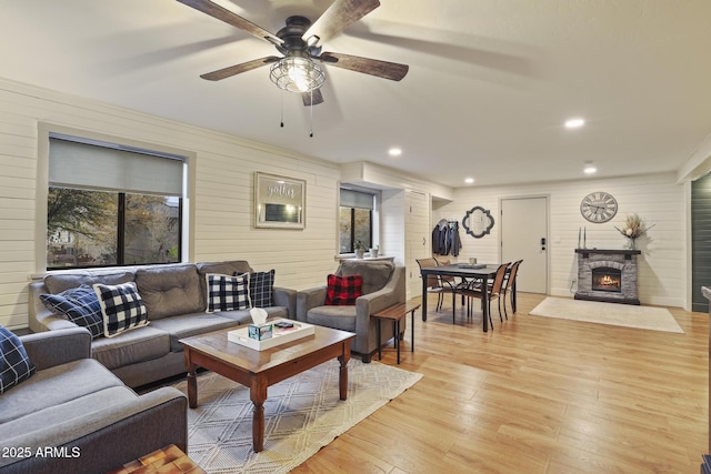 living room featuring wooden walls, light wood finished floors, a fireplace, a ceiling fan, and recessed lighting