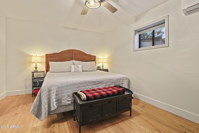 bedroom featuring an AC wall unit, baseboards, wood finished floors, and ceiling fan