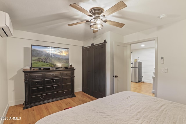 bedroom featuring freestanding refrigerator, light wood-type flooring, a barn door, baseboards, and a wall mounted air conditioner