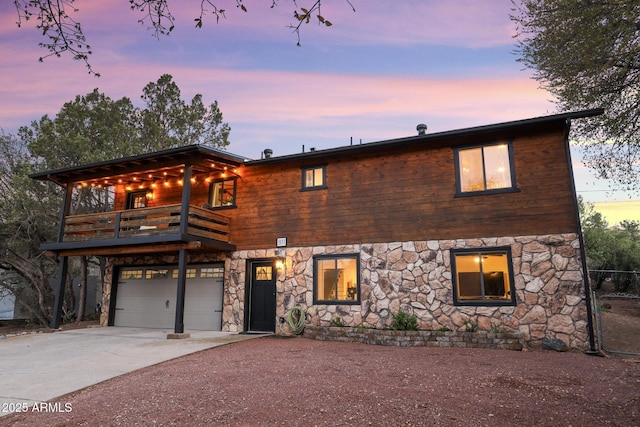 view of front of home with driveway, stone siding, a balcony, and an attached garage