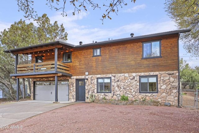 chalet / cabin with a balcony, concrete driveway, stone siding, and a garage