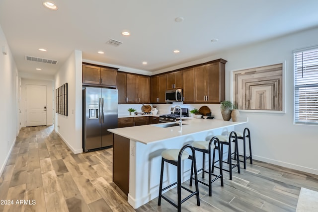 kitchen featuring sink, stainless steel appliances, kitchen peninsula, light hardwood / wood-style floors, and a kitchen bar