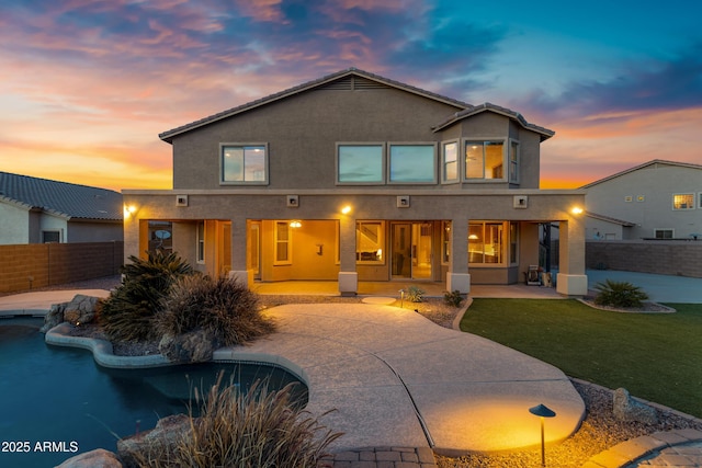 back house at dusk with a fenced in pool, a yard, and a patio