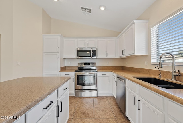 kitchen with vaulted ceiling, appliances with stainless steel finishes, sink, white cabinets, and light tile patterned floors