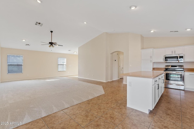 kitchen featuring lofted ceiling, light tile patterned floors, appliances with stainless steel finishes, a center island, and white cabinets