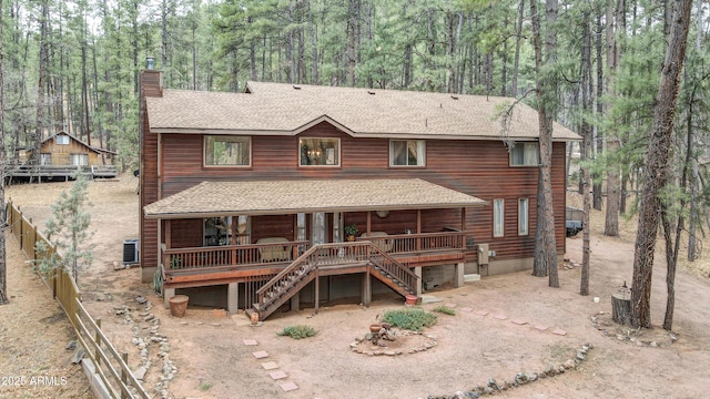 chalet / cabin featuring a chimney, a shingled roof, a porch, a wooded view, and stairs