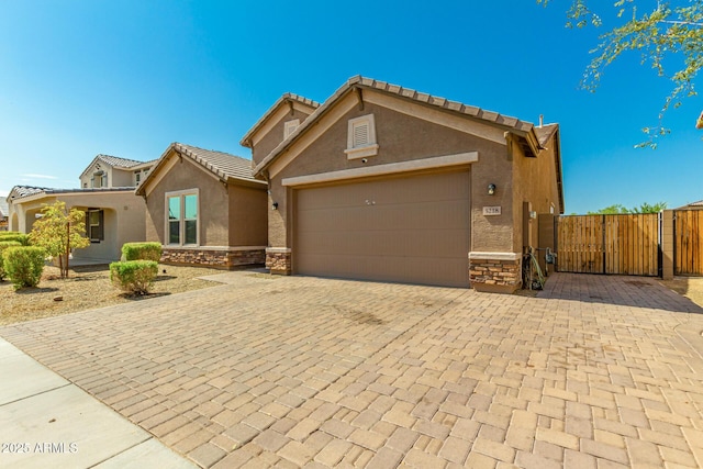 5218 W Lydia Ln, Laveen, AZ 85339 - view of front of house featuring stucco siding, stone siding, decorative driveway, an attached garage, and a gate