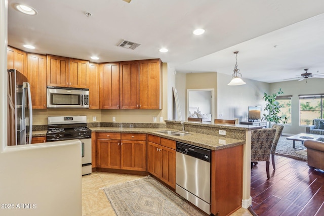 kitchen featuring pendant lighting, sink, dark stone counters, kitchen peninsula, and stainless steel appliances