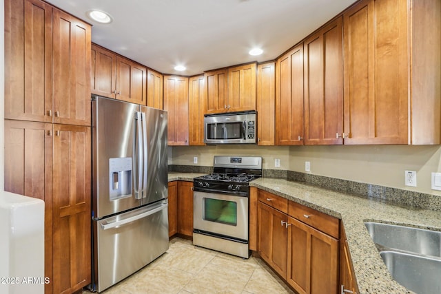 kitchen with stainless steel appliances, light stone countertops, sink, and light tile patterned floors