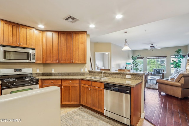 kitchen with sink, light stone counters, pendant lighting, stainless steel appliances, and hardwood / wood-style floors