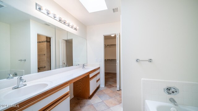 bathroom featuring tile patterned floors, vanity, a tub, and a skylight